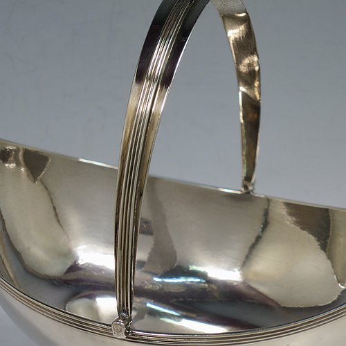 An Antique Georgian Sterling Silver sugar basket, having a plain oval bellied body, with applied reeded borders, a hinged and reeded swing-handle, and sitting on a pedestal foot. Made by Peter & Anne Bateman of London in 1798. The dimensions of this fine hand-made antique silver sugar basket are height (inc. handle) 18 cms (7 inches), length 16.6 cms (6.5 inches), and it weighs approx. 215g (7 troy ounces).