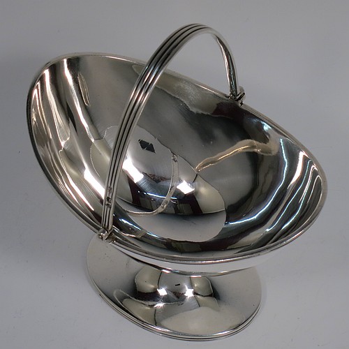An Antique Victorian Sterling Silver sugar basket in a Georgian style, having a plain oval shaped body, with applied reeded borders, a reeded swing-handle, and sitting on a pedestal foot. Made by Holland, Aldwinckle, and Slater of London in 1895. The dimensions of this fine hand-made antique silver sugar basket are height 14.5 cms (5.75 inches), length 13 cms (5 inches), width 9.5 cms (3.75 inches), and it weighs approx. 188g (6 troy ounces).