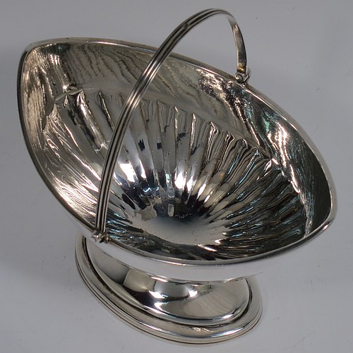 An Antique Georgian Sterling Silver sugar basket, having an oval bellied body with hand-chased half-fluting, with applied reeded borders, a hinged and reeded swing-handle, and sitting on a pedestal foot. Made by Peter & Anne Bateman of London in 1791. The dimensions of this fine hand-made antique silver sugar basket are height (inc. handle) 15 cms (6 inches), length 14 cms (5.5 inches), and it weighs approx. 198g (6.4 troy ounces).