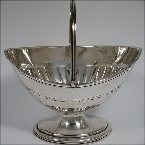 An Antique Georgian Sterling Silver sugar basket, having an oval bellied body with hand-chased half-fluting, with applied reeded borders, a hinged and reeded swing-handle, and sitting on a pedestal foot. Made by Peter & Anne Bateman of London in 1791. The dimensions of this fine hand-made antique silver sugar basket are height (inc. handle) 15 cms (6 inches), length 14 cms (5.5 inches), and it weighs approx. 198g (6.4 troy ounces).