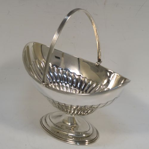 A very pretty Antique Victorian Sterling Silver sugar basket, having an oval body with tapering sides and hand-chased half-fluted decoration, with an applied reeded top border, a hinged and reeded swing-handle, and sitting on a plain oval stepped pedestal foot. This beautiful antique silver sweet-meat basket was made by Thomas Bradbury of London in 1897. The dimensions of this fine hand-made antique silver sugar basket are height (inc. handle) 13.5 cms (5.3 inches), length 13.5 cms (5.3 inches), width 9.5 cms (3.75 inches), and it weighs approx. 132g (4.3 troy ounces).