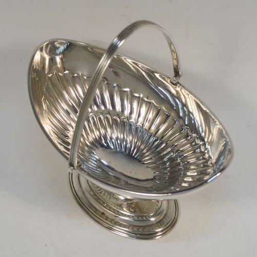 A very pretty Antique Victorian Sterling Silver sugar basket, having an oval body with tapering sides and hand-chased half-fluted decoration, with an applied reeded top border, a hinged and reeded swing-handle, and sitting on a plain oval stepped pedestal foot. This beautiful antique silver sweet-meat basket was made by Thomas Bradbury of London in 1897. The dimensions of this fine hand-made antique silver sugar basket are height (inc. handle) 13.5 cms (5.3 inches), length 13.5 cms (5.3 inches), width 9.5 cms (3.75 inches), and it weighs approx. 132g (4.3 troy ounces).
