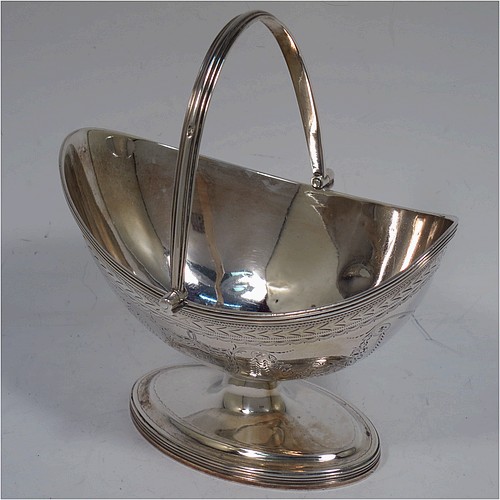 A very pretty Antique Georgian Sterling Silver sugar basket, having an oval bellied body in a Neoclassical style with hand-engraved floral and swag decoration, applied reeded borders, a hinged and reeded swing-handle, and sitting on a pedestal foot. Made by Henry Chawner of London in 1790. The dimensions of this fine hand-made antique silver sugar basket are height (inc. handle) 12.5 cms (5 inches), length 12.5 cms (5 inches), and it weighs approx. 151g (4.9 troy ounces).