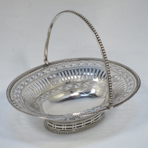 A very pretty Antique Georgian Sterling Silver sugar or sweetmeat basket, having an oval body, with hand-pierced neoclassical style decoration, an applied bead-edged border, a beeded swing-handle, and sitting on a matching pedestal foot. Made by Robert Hennell of London in 1781. The dimensions of this fine hand-made antique silver sweet-meat or sugar basket are height 13 cms (5 inches), length 15.5 cms (6 inches), width 12.5 cms (5 inches), and it weighs approx. 156g (5 troy ounces).  
