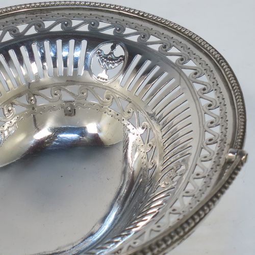 A very pretty Antique Georgian Sterling Silver sugar or sweetmeat basket, having an oval body, with hand-pierced neoclassical style decoration, an applied bead-edged border, a beeded swing-handle, and sitting on a matching pedestal foot. Made by Robert Hennell of London in 1781. The dimensions of this fine hand-made antique silver sweet-meat or sugar basket are height 13 cms (5 inches), length 15.5 cms (6 inches), width 12.5 cms (5 inches), and it weighs approx. 156g (5 troy ounces).