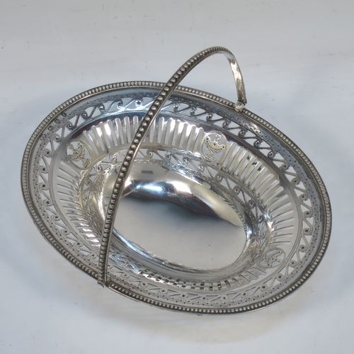 A very pretty Antique Georgian Sterling Silver sugar or sweetmeat basket, having an oval body, with hand-pierced neoclassical style decoration, an applied bead-edged border, a beeded swing-handle, and sitting on a matching pedestal foot. Made by Robert Hennell of London in 1781. The dimensions of this fine hand-made antique silver sweet-meat or sugar basket are height 13 cms (5 inches), length 15.5 cms (6 inches), width 12.5 cms (5 inches), and it weighs approx. 156g (5 troy ounces).