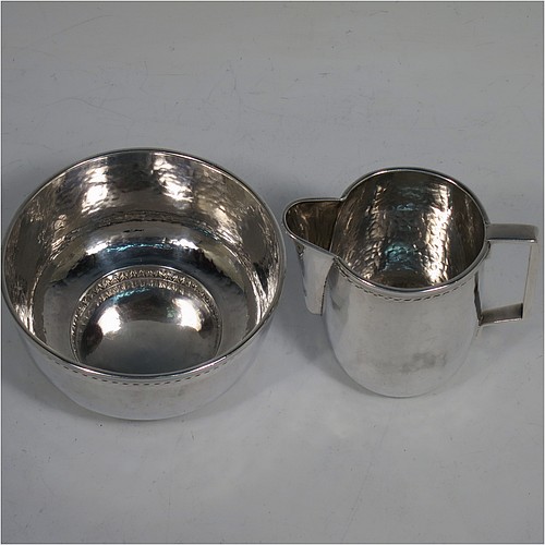 A very attractive Arts and Crafts Sterling Silver sugar and creamer set, having round bodies with hand-hammered plenished decoration, with applied reeded and rope-twist top borders, all sitting on flat bases. Made by Edward Spencer of the Artificiers Guild of London in 1928. The dimensions of this fine hand-made Arts and Crafts silver sugar and creamer set are diameter of sugar bowl 9 cms (3.5 inches), height of cream jug 7 cms (2.75 inches), with a total weight of 173g (5.6 troy ounces).