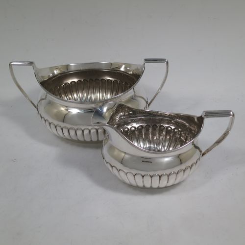 A very handsome Antique Georgian Irish Sterling Silver sugar bowl and cream jug set, having oval bellied bodies with hand-chased half-fluted decoration, applied reeded borders and flat-topped side-handles, and all sitting on collet feet. Made by James Scott of Dublin in 1806. The dimensions of this fine hand-made antique Irish silver sugar and creamer set are length of sugar bowl (inc. handles) 20 cms (8 inches), height 10 cms (4 inches), width 13 cms (5 inches), with a total weight of approx. 436g (14 troy ounces).    