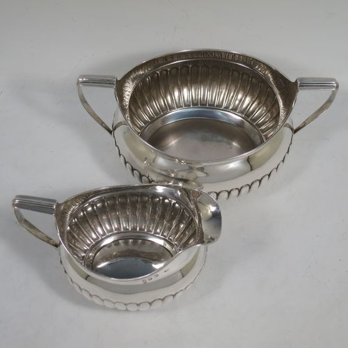 A very handsome Antique Georgian Irish Sterling Silver sugar bowl and cream jug set, having oval bellied bodies with hand-chased half-fluted decoration, applied reeded borders and flat-topped side-handles, and all sitting on collet feet. Made by James Scott of Dublin in 1806. The dimensions of this fine hand-made antique Irish silver sugar and creamer set are length of sugar bowl (inc. handles) 20 cms (8 inches), height 10 cms (4 inches), width 13 cms (5 inches), with a total weight of approx. 436g (14 troy ounces).    