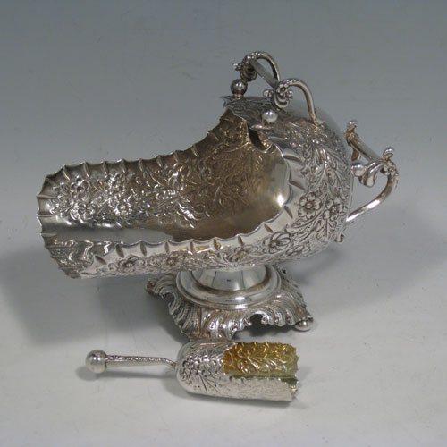 Antique Victorian sterling silver sugar scuttle, having a hand-chased body with floral decoration, two cast twin-scroll handles, an original scoop with gold-gilt interior, and sitting on a pedestal foot with four cushion feet. Made by Walker and Hall of Birmingham in 1899. Length 16 cms (6.25 inches), height 12.5 cms (5 inches), width 8 cms (3 inches). Weight approx. 216g (7 troy ounces).