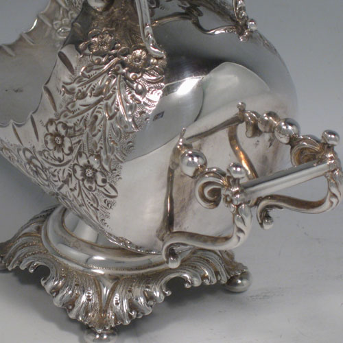 Antique Victorian sterling silver sugar scuttle, having a hand-chased body with floral decoration, two cast twin-scroll handles, an original scoop with gold-gilt interior, and sitting on a pedestal foot with four cushion feet. Made by Walker and Hall of Birmingham in 1899. Length 16 cms (6.25 inches), height 12.5 cms (5 inches), width 8 cms (3 inches). Weight approx. 216g (7 troy ounces).