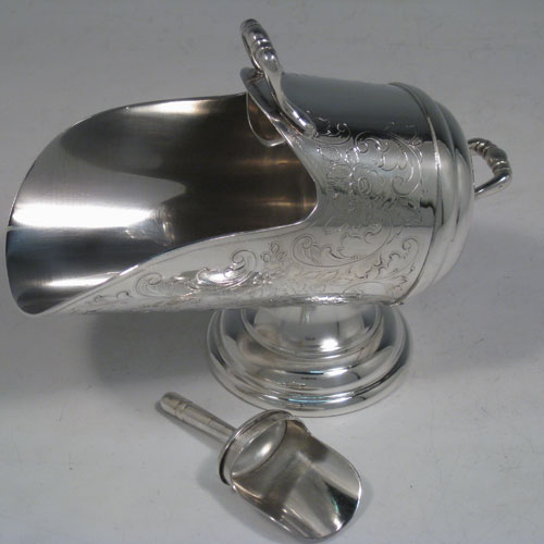 Antique Victorian silver-plated sugar scuttle, having a hand-engraved body with floral decoration, two cast scroll handles, an original scoop, and sitting on a pedestal foot. Made in ca. 1890. The dimensions of this fine hand-made silver-plated sugar scuttle are length 15 cms (6 inches), height 11.5 cms (4.5 inches), and width 7.5 cms (3 inches).