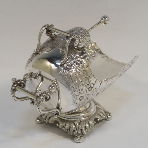 A rare and very pretty Antique Victorian Sterling Silver sugar scuttle, having a hand-chased body with floral decoration, two cast twin-scroll handles, an original scoop, and sitting on a pedestal foot with four cushion feet. This beautiful antique silver sugar scuttle was made by William Davenport of Birmingham in 1900. The dimensions of this fine hand-made silver sugar scuttle are length 15 cms (6 inches), height 12 cms (4.75 inches), width 8 cms (3 inches), and it weighs approx. 209g (6.7 troy ounces).