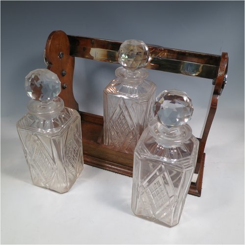 An Antique Edwardian silver plated and wood-framed three bottle tantalus, with hand-cut crystal decanters and stoppers, all mounted in an oak frame with silver-plated swing handle, a patented lock mechanism, and hand-cut silver-plated mounts. Made in ca. 1905. The dimensions of this fine hand-made antique silver-plated and wooden framed tantalus are height 34 cms (13.5 inches), length , width 37 cms (14.5 inches), and width 14 cms (5.5 inches). Please note that shipping and insurance would be extra for this item so please check with us first before ordering.