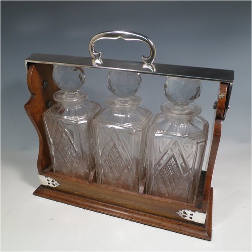 An Antique Edwardian silver plated and wood-framed three bottle tantalus, with hand-cut crystal decanters and stoppers, all mounted in an oak frame with silver-plated swing handle, a patented lock mechanism, and hand-cut silver-plated mounts. Made in ca. 1905. The dimensions of this fine hand-made antique silver-plated and wooden framed tantalus are height 34 cms (13.5 inches), length , width 37 cms (14.5 inches), and width 14 cms (5.5 inches). Please note that shipping and insurance would be extra for this item so please check with us first before ordering.