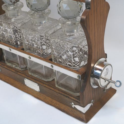 A very handsome Antique Silver-plated and wood framed three-bottle tantalus, with original hand-cut crystal decanters and stoppers, all in an oak (poss.) wooden frame with silver-plated and nickel pinned mounts, with a patented lock mechanism and key. The presentation inscription is engraved onto a sterling silver plaque with hallmarks, which indicate that this beautiful antique silver-plated and wood tantalus was made by Walker and Hall of Birmingham in 1912. The dimensions of this fine hand-made antique three-bottle tantalus are length 36 cms (14 inches), height 32 cms (12.5 inches), and depth 14 cms (5.5 inches).