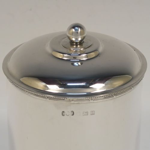 A very handsome Antique Sterling Silver tea caddy box, having a plain cylindrical body with straight sides and applied bead, ribbon and reed top and bottom borders, a slightly domed lift-off lid with a ball finial, and sitting on a flat base. This elegant silver tea caddy box was made by Hukin and Heath of Birmingham in 1924. The dimensions of this fine hand-made antique silver tea caddy box are height 13 cms ( 5inches), diameter 9 cms (3.5 inches), and it weighs approx. 255g (8.2 troy ounces).