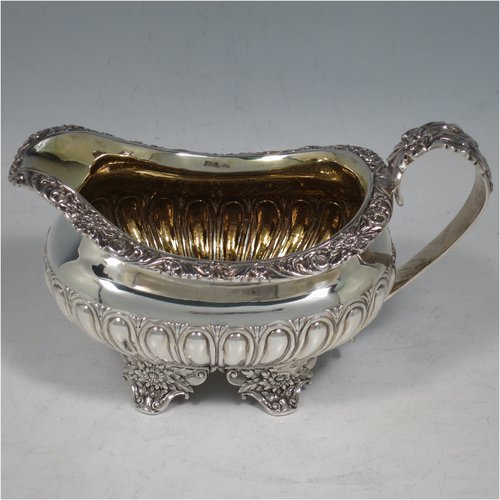 An Antique Georgian Sterling Silver three-piece Regency style tea set, having a teapot, sugar bowl and cream jug. The bodies all hand-chased with half-fluted decoration, the sugar and creamer with gold-gilt interiors, the teapot with silver handle and finial, and an invisibly hinged lid, all with applied cast acanthus leaf and floral borders, and all sitting on four floral cast flange feet. Made by Joseph Angell of London in 1824. The dimensions of this fine hand-made antique silver tea service are length of teapot 30.5 cms (12 inches), height 16 cms (6.3 inches), and it weighs a total of approx. 1,395g (45 troy ounces).   