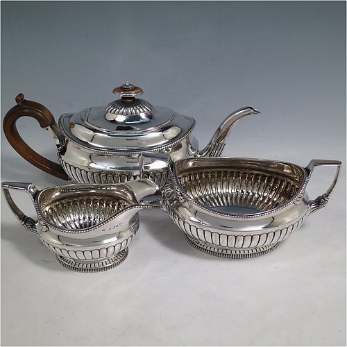 An Antique Georgian Sterling Silver three-piece early Regency style tea set, having a teapot, sugar bowl and cream jug. The oval bodies all hand-chased with half-fluted decoration, the sugar and creamer with gold-gilt interiors, the teapot with wooden handle and finial, and an invisibly hinged lid, all with applied gadroon borders, and all sitting on pedestal feet. Made by Daniel Pontifex London in 1805. The dimensions of this fine hand-made antique silver tea service are length of teapot 30 cms (11.75 inches), height 15 cms (6 inches), and it weighs a total of approx. 1,170g (38 troy ounces).    
