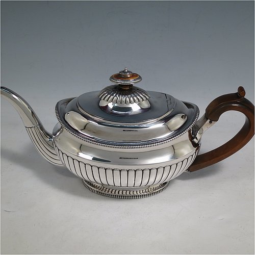 An Antique Georgian Sterling Silver three-piece early Regency style tea set, having a teapot, sugar bowl and cream jug. The oval bodies all hand-chased with half-fluted decoration, the sugar and creamer with gold-gilt interiors, the teapot with wooden handle and finial, and an invisibly hinged lid, all with applied gadroon borders, and all sitting on pedestal feet. Made by Daniel Pontifex London in 1805. The dimensions of this fine hand-made antique silver tea service are length of teapot 30 cms (11.75 inches), height 15 cms (6 inches), and it weighs a total of approx. 1,170g (38 troy ounces).