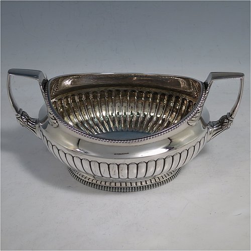 An Antique Georgian Sterling Silver three-piece early Regency style tea set, having a teapot, sugar bowl and cream jug. The oval bodies all hand-chased with half-fluted decoration, the sugar and creamer with gold-gilt interiors, the teapot with wooden handle and finial, and an invisibly hinged lid, all with applied gadroon borders, and all sitting on pedestal feet. Made by Daniel Pontifex London in 1805. The dimensions of this fine hand-made antique silver tea service are length of teapot 30 cms (11.75 inches), height 15 cms (6 inches), and it weighs a total of approx. 1,170g (38 troy ounces).