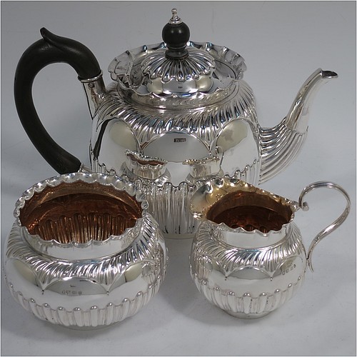 A very pretty Antique Victorian Sterling Silver three-piece bachelor tea set, having round bellied bodies with beautiful bands of hand-chased fluted decoration and wavy top borders, the teapot with a hinged lid and wooden finial, a wooden scroll handle, and the cream and sugar bowl with gold-gilt interiors, all sitting on collet feet. Made by Thomas Hayes of Birmingham in 1888. The dimensions of this fine hand-made antique silver bachelor tea set are height of teapot 14 cms (5.5 inches), length of teapot 19 cms (7.5 inches), with a total weight of approx. 474g (15.3 troy ounces).    