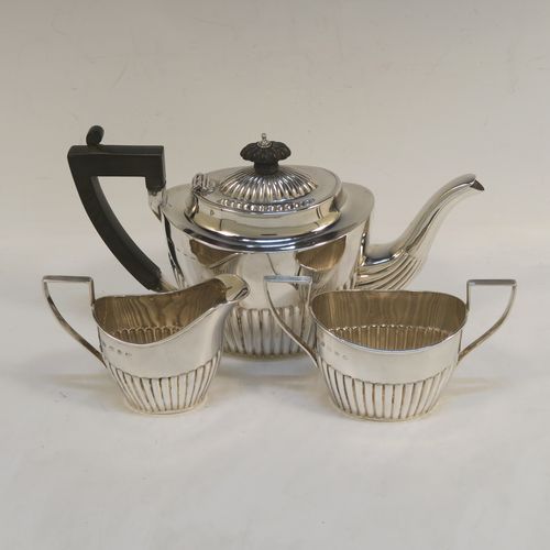A handsome Antique Sterling Silver Bachelor three-piece tea set, having oval shaped bodies, with half-fluted hand-chased decoration, with reeded handles on the sugar & cream jug, a wooden handle and finial on the teapot, and all sitting on flat bases. This beautiful antique silver bachelor tea set was all made by John Milward Banks of Birmingham in 1896. The dimensions of this fine hand-made antique silver bachelor tea set are length of teapot 21.5 cms (8.5 inches), height 12.5 cms (5 inches), and the total weight is approx. 320g (10.3 troy ounces).  
