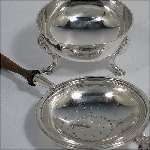 A very handsome, large, and heavy Sterling Silver tea strainer and bowl, having a plain wood-turned handle, a round hand-pierced bowl with an applied reeded border and a cast shell side holder, and sitting on a plain round dregs bowl with three cast hoof feet and shell shoulders. Made by Robert Comyns of London in 1964. The dimensions of this fine hand-made silver tea strainer & bowl are length 19 cms (7.5 inches), diameter of bowl 8 cms (3 inches), with a total weight of approx. 155g (5 troy ounces).