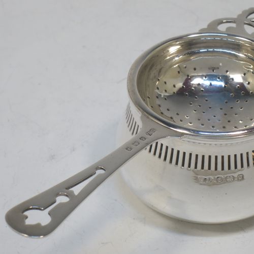 A pretty Sterling Silver tea strainer and bowl, having a hand-pierced handle, a round hand-pierced bowl with hand-cut side holder, and sitting on a plain round dregs stand with a band of piercing and bellied sides. Made by William Suckling Ltd., of Birmingham in 1933. The dimensions of this fine hand-made silver tea strainer & stand are length 14.5 cms (5.75 inches), diameter of stand 6 cms (2.3 inches), with a total weight of approx. 75g (2.4 troy ounces).  