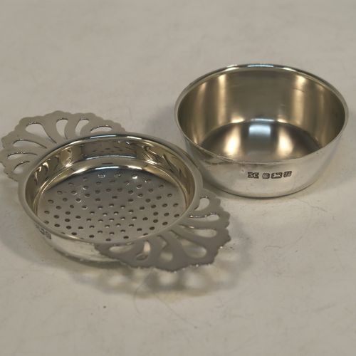 A handsome Sterling Silver tea strainer and dregs bowl in a Georgian lemon strainer style, having a round hand-pierced bowl, with two hand-pierced side-handles, and sitting on an original plain round dregs stand with a flat base. Made by S. C. of Sheffield in 1976. The dimensions of this fine hand-made silver tea strainer and bowl are height 2.5 cms (1 inch), width across handles 11 cms (4.25 inches), and it weighs a total of approx. 78g (2.5 troy ounces).  