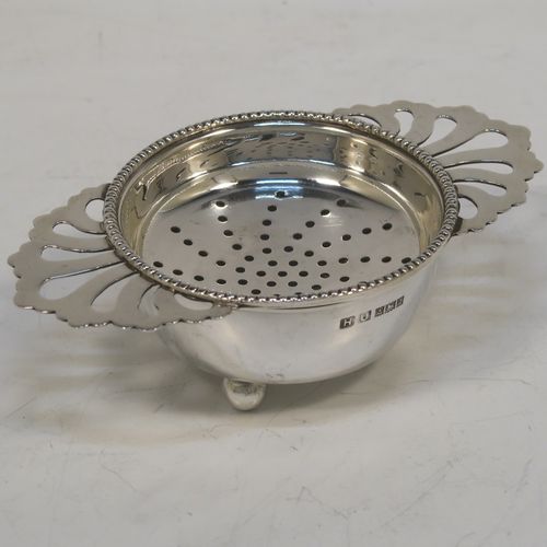 An elegant Sterling Silver tea strainer and dregs bowl in a Georgian lemon strainer style, having a round hand-pierced bowl with an applied bead-edged border, with two hand-pierced side-handles, and sitting on an original plain round dregs stand with three ball feet. This beautiful silver tea strainer was made by Hampton Utilities of Birmingham in 1965. The dimensions of this fine hand-made silver tea strainer and bowl are height 3.5 cms (1.3 inches), width across handles 11 cms (4.25 inches), diameter of bowl 6.5 cms (2.5 inches), and it weighs a total of approx. 87g (2.8 troy ounces).   