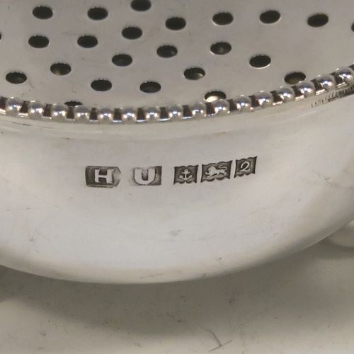 An elegant Sterling Silver tea strainer and dregs bowl in a Georgian lemon strainer style, having a round hand-pierced bowl with an applied bead-edged border, with two hand-pierced side-handles, and sitting on an original plain round dregs stand with three ball feet. This beautiful silver tea strainer was made by Hampton Utilities of Birmingham in 1965. The dimensions of this fine hand-made silver tea strainer and bowl are height 3.5 cms (1.3 inches), width across handles 11 cms (4.25 inches), diameter of bowl 6.5 cms (2.5 inches), and it weighs a total of approx. 87g (2.8 troy ounces).