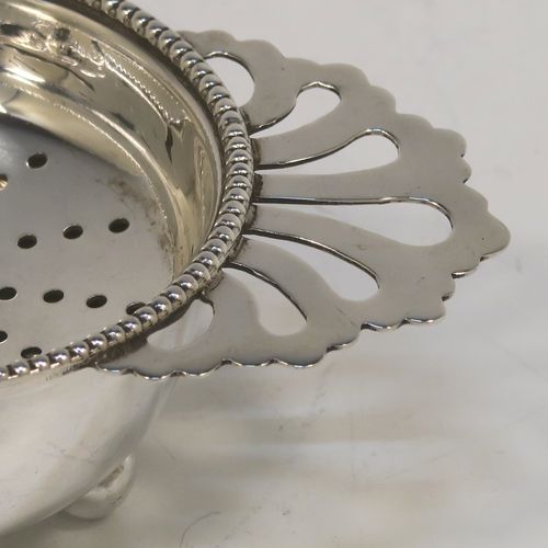 An elegant Sterling Silver tea strainer and dregs bowl in a Georgian lemon strainer style, having a round hand-pierced bowl with an applied bead-edged border, with two hand-pierced side-handles, and sitting on an original plain round dregs stand with three ball feet. This beautiful silver tea strainer was made by Hampton Utilities of Birmingham in 1965. The dimensions of this fine hand-made silver tea strainer and bowl are height 3.5 cms (1.3 inches), width across handles 11 cms (4.25 inches), diameter of bowl 6.5 cms (2.5 inches), and it weighs a total of approx. 87g (2.8 troy ounces).