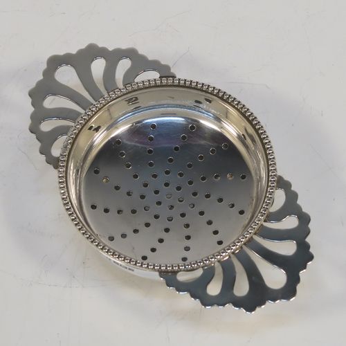 An elegant Sterling Silver tea strainer and dregs bowl in a Georgian lemon strainer style, having a round hand-pierced bowl with an applied bead-edged border, with two hand-pierced side-handles, and sitting on an original plain round dregs stand with three ball feet. This beautiful silver tea strainer was made by Hampton Utilities of Birmingham in 1965. The dimensions of this fine hand-made silver tea strainer and bowl are height 3.5 cms (1.3 inches), width across handles 11 cms (4.25 inches), diameter of bowl 6.5 cms (2.5 inches), and it weighs a total of approx. 87g (2.8 troy ounces).