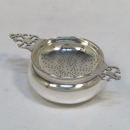 A handsome Sterling Silver tea strainer and dregs bowl in a Georgian lemon strainer style, having a round hand-pierced bowl, with two hand-pierced side-handles, and sitting on an original plain round dregs stand with a reeded border and flat base. This elegant silver tea strainer and bowl was made by Robert Comyns of London in 1940. The dimensions of this fine hand-made silver tea strainer and bowl are height 3.5 cms (1.3 inches), length across handles 12 cms (4.75 inches), and it weighs a total of approx. 80g (2.6 troy ounces).   