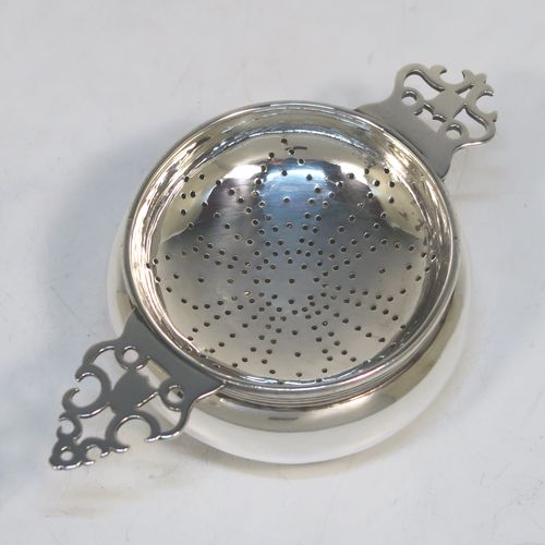 A handsome Sterling Silver tea strainer and dregs bowl in a Georgian lemon strainer style, having a round hand-pierced bowl, with two hand-pierced side-handles, and sitting on an original plain round dregs stand with a reeded border and flat base. This elegant silver tea strainer and bowl was made by Robert Comyns of London in 1940. The dimensions of this fine hand-made silver tea strainer and bowl are height 3.5 cms (1.3 inches), length across handles 12 cms (4.75 inches), and it weighs a total of approx. 80g (2.6 troy ounces).   