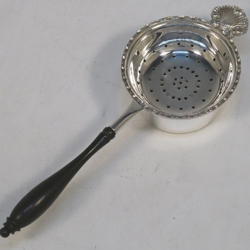 A very pretty Sterling Silver tea strainer and bowl, having a plain black stained wood-turned handle, a round hand-pierced bowl with an applied floral border and a cast shell side holder, and sitting on a plain round dregs bowl with a flat base. This beautiful silver tea strainer and bowl were made by Francis Howard of Sheffield in 1984. The dimensions of this fine hand-made silver tea strainer & bowl are length 18 cms (7 inches), diameter of bowl 6.5 cms (2.5 inches), and with a total weight of approx. 90g (3 troy ounces).  