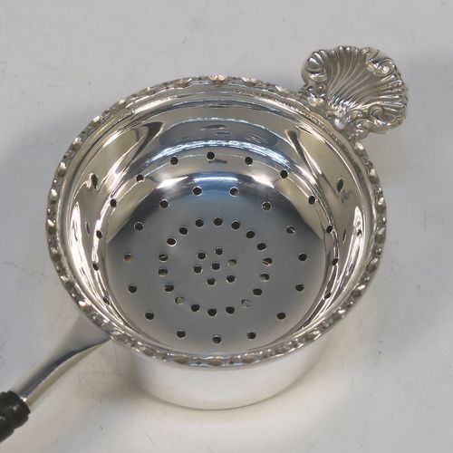 A very pretty Sterling Silver tea strainer and bowl, having a plain black stained wood-turned handle, a round hand-pierced bowl with an applied floral border and a cast shell side holder, and sitting on a plain round dregs bowl with a flat base. This beautiful silver tea strainer and bowl were made by Francis Howard of Sheffield in 1984. The dimensions of this fine hand-made silver tea strainer & bowl are length 18 cms (7 inches), diameter of bowl 6.5 cms (2.5 inches), and with a total weight of approx. 90g (3 troy ounces).  