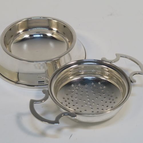 A handsome Antique Sterling Silver tea strainer and dregs bowl in a Georgian lemon strainer style, having a round hand-pierced bowl, with two side-handles, and sitting on an original plain round dregs stand. This elegant antique silver tea strainer and bowl was made by J. B. Carrington of Birmingham in 1921. The dimensions of this fine hand-made silver tea strainer and dregs stand are height 2.5 cms (1 inch), diameter of dregs stand  9.5 cms (3.75 inches), and it weighs a total of approx. 117g (3.8 troy ounces).  