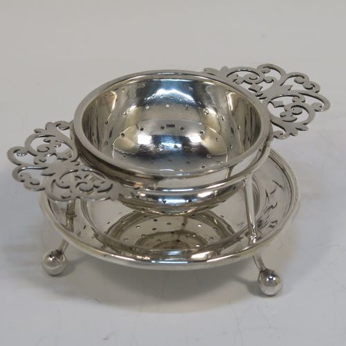 A very stylish Antique Sterling Silver tea strainer and stand, having a round hand-pierced bowl with two florally pierced side-handles, all sitting on an original plain round dregs stand with a wire-work galleried holder on a base with three ball feet. This elegant antique silver tea strainer and stand was made by George Howson of Sheffield in 1920. The dimensions of this fine hand-made antique silver tea strainer and stand are height 4 cms (1.5 inches), length over handles 10 cms (4 inches), and it weighs a total of approx. 80g (2.6 troy ounces).  