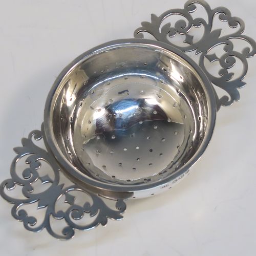 A very stylish Antique Sterling Silver tea strainer and stand, having a round hand-pierced bowl with two florally pierced side-handles, all sitting on an original plain round dregs stand with a wire-work galleried holder on a base with three ball feet. This elegant antique silver tea strainer and stand was made by George Howson of Sheffield in 1920. The dimensions of this fine hand-made antique silver tea strainer and stand are height 4 cms (1.5 inches), length over handles 10 cms (4 inches), and it weighs a total of approx. 80g (2.6 troy ounces).