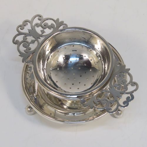 A very stylish Antique Sterling Silver tea strainer and stand, having a round hand-pierced bowl with two florally pierced side-handles, all sitting on an original plain round dregs stand with a wire-work galleried holder on a base with three ball feet. This elegant antique silver tea strainer and stand was made by George Howson of Sheffield in 1920. The dimensions of this fine hand-made antique silver tea strainer and stand are height 4 cms (1.5 inches), length over handles 10 cms (4 inches), and it weighs a total of approx. 80g (2.6 troy ounces).