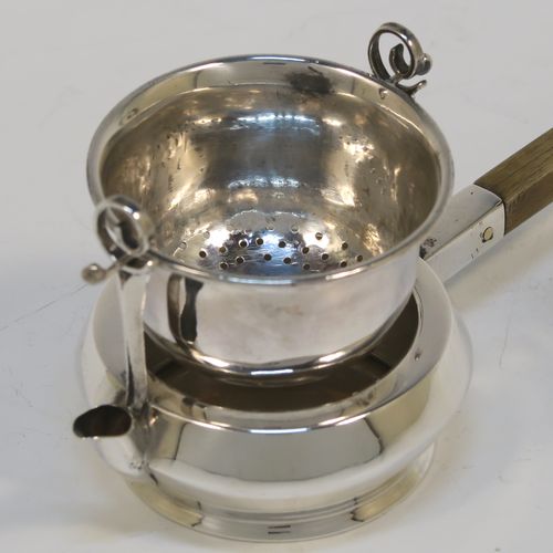 A very unusual Antique Edwardian Sterling Silver gimble-mounted tea strainer on a teapot style stand, having a round hand-pierced bowl mounted on two side stands, all sitting on an original plain round dregs stand in the shape of a teapot, together with an original wooden insulated side-handle. This rare antique silver tea strainer and stand was made by Fredericks Ltd., of London in 1907. The dimensions of this fine hand-made antique silver tea strainer and stand are height 5.5 cms (2.25 inches), length including handle 17 cms (6.75 inches), and it weighs a total of approx. 50g (1.6 troy ounces).   