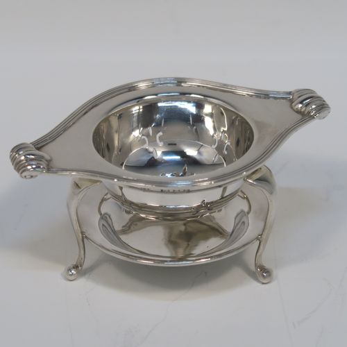 A very stylish Antique Sterling Silver tea strainer and stand, having a round hand-pierced bowl with an applied reeded border and side-handles, all sitting on an original plain round dregs stand with a wire-work galleried holder  with three cabriolet legs. This elegant silver tea strainer and stand was made by Robert Pringle of London in 1928. The dimensions of this fine hand-made silver tea strainer and stand are height 4 cms (1.5 inches), length over handles 10 cms (4 inches), and it weighs a total of approx. 77g (2.5 troy ounces).   