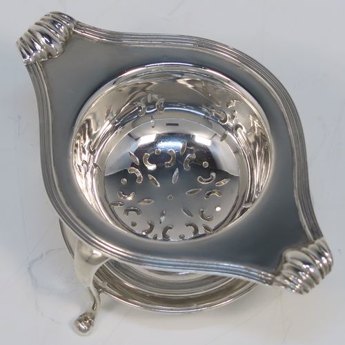 A very stylish Antique Sterling Silver tea strainer and stand, having a round hand-pierced bowl with an applied reeded border and side-handles, all sitting on an original plain round dregs stand with a wire-work galleried holder  with three cabriolet legs. This elegant silver tea strainer and stand was made by Robert Pringle of London in 1928. The dimensions of this fine hand-made silver tea strainer and stand are height 4 cms (1.5 inches), length over handles 10 cms (4 inches), and it weighs a total of approx. 77g (2.5 troy ounces).   