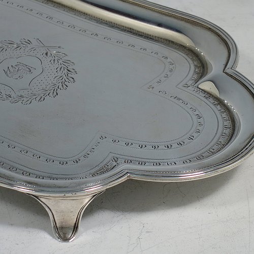 An Antique Georgian Sterling Silver Neoclassical style teapot stand having a lobed rectangular body with a raised edge and applied reeded border, a hand-engraved ground with floral bands of decoration and a central cartouche with laurel-leaf surround, and all sitting on four flange feet. Made by Henry Chawner of London in 1792. The dimensions of this fine hand-made antique silver teapot stand are length 20 cms (8 inches), width 13 cms (5.25 inches), and it weighs approx. 191g (6 troy ounces). Please note that this item is crested.