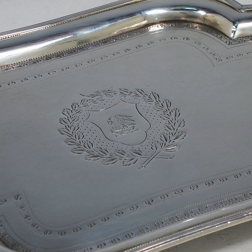 An Antique Georgian Sterling Silver Neoclassical style teapot stand having a lobed rectangular body with a raised edge and applied reeded border, a hand-engraved ground with floral bands of decoration and a central cartouche with laurel-leaf surround, and all sitting on four flange feet. Made by Henry Chawner of London in 1792. The dimensions of this fine hand-made antique silver teapot stand are length 20 cms (8 inches), width 13 cms (5.25 inches), and it weighs approx. 191g (6 troy ounces). Please note that this item is crested.