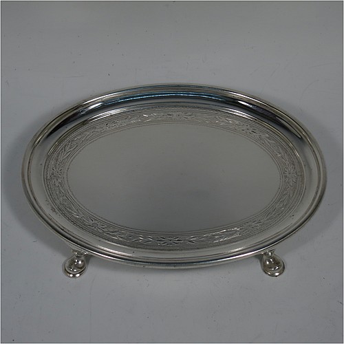 A very handsome Antique Edwardian Sterling Silver teapot stand, having an oval body with a band of hand-engraved floral decoration, a raised border with an applied reeded edge, and sitting on four cast hoof feet. Made by the Pairpoint Brothers of London in 1905. The dimensions of this fine hand-made antique silver teapot stand are length 17.5 cms (7 inches), width 13 cms (5 inches), and it weighs approx. 238g (7.8 troy ounces).