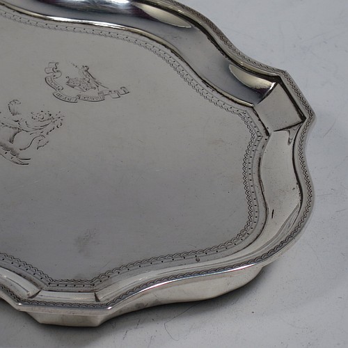 A very handsome Antique Georgian Sterling Silver teapot stand, having a shaped and cut-cornered oval body with an applied and engraved border, the flat ground with a hand-engraved band of stipple-work, and all sitting on a flat wooden base with green felt cover. Made by John Denziloe of London in 1791. The dimensions of this fine hand-made antique silver teapot stand are length 17 cms (6.75 inches), and width 13 cms (5 inches). Please note that this item is crested.