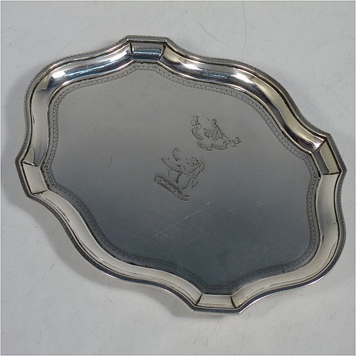 A very handsome Antique Georgian Sterling Silver teapot stand, having a shaped and cut-cornered oval body with an applied and engraved border, the flat ground with a hand-engraved band of stipple-work, and all sitting on a flat wooden base with green felt cover. Made by John Denziloe of London in 1791. The dimensions of this fine hand-made antique silver teapot stand are length 17 cms (6.75 inches), and width 13 cms (5 inches). Please note that this item is crested.